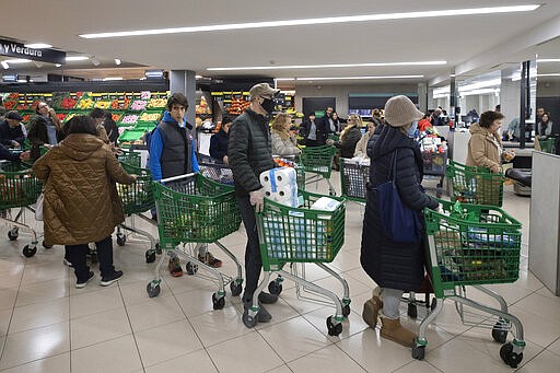 Customers, some with protective masks, queue at the check out of a supermarket as people begin to stock up on provisions in Madrid, Spain, Tuesday, March 10, 2020. Spain's health minister on Monday announced a sharp spike in coronavirus cases in and around the national capital, Madrid, and said all schools in the region, including kindergartens and universities, will close for two weeks from Wednesday. (AP Photo/Paul White)