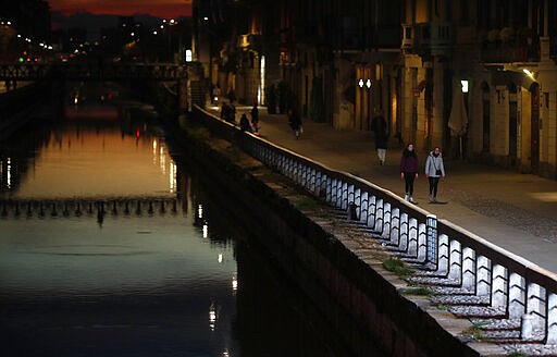 Few people walk at the Naviglio Grande canal, one of the favorite spots for night life in Milan, Italy, Tuesday, March 10, 2020. Italy entered its second day under a nationwide lockdown after a government decree extended restrictions on movement from the hard-hit north to the rest of the country to prevent the spreading of coronavirus. For most people, the new coronavirus causes only mild or moderate symptoms, such as fever and cough. For some, especially older adults and people with existing health problems, it can cause more severe illness, including pneumonia. (AP Photo/Antonio Calanni)