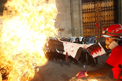 Riot police hold the line as they are attacked with gasoline bomb at the door of the National Palace during an International Women's Day march in Mexico City's main square, the Zocalo, Sunday, March 8, 2020. Protests against gender violence in Mexico have intensified in recent years amid an increase in killings of women and girls.(AP Photo/Rebecca Blackwell)