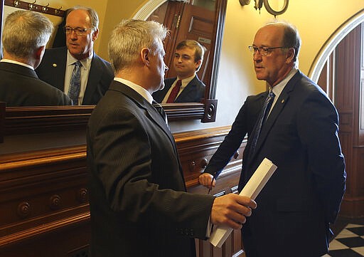 FILE -  In this Wednesday, Feb. 26, 2020 file photo, Senate Vice President Jeff Longbine, R-Emporia, right, speaks with Tim Graham, left, a member of Democratic Gov. Laura Kelly's staff, outside the Senate chamber, at the Statehouse in Topeka, Kan. Pictured in the center in the mirror is Michael Murray, Longbine's chief of staff. A new legislative proposal would increase the budgets of legislative leaders' offices, with the biggest increases going to Longbine's office and the House speaker pro tem's office. (AP Photo/John Hanna, File)