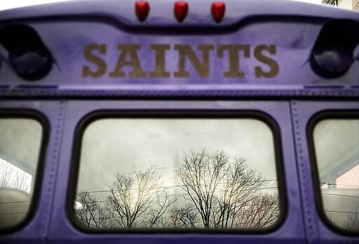 In this March 6, 2020, photo, a school bus sits vacant while parked at Saint Raphael Academy in Pawtucket, R.I., as the school remains closed following a confirmed case of the coronavirus. As a growing number of schools across the United States close their doors because of the coronavirus, officials are weighing whether to shut down entirely or move classes online, which could leave behind the many students who don't have computers, home internet access or parents with flexible work schedules. (AP Photo/David Goldman)