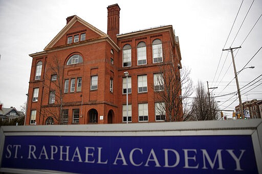 In this March 6, 2020, photo, Saint Raphael Academy stands in the background in Pawtucket, R.I., as the school remains closed following a confirmed case of the coronavirus. As a growing number of schools across the United States close their doors because of the coronavirus, officials are weighing whether to shut down entirely or move classes online, which could leave behind the many students who don't have computers, home internet access or parents with flexible work schedules. (AP Photo/David Goldman)