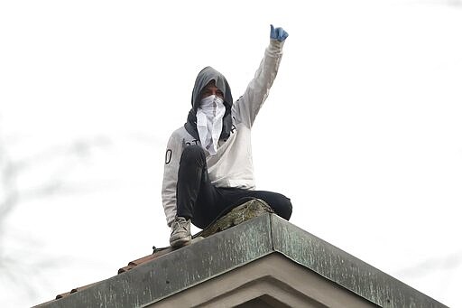 A man stands on the roof of the San Vittore prison during a protest in Milan, Italy, Monday, March 9, 2020. Italian penitentiary police say six inmates protesting virus containment measures at a northern Italian prison have died after they broke into the infirmary and overdosed on methadone. The protest Sunday in Modena was among the first of more than two-dozen riots at Italy&#146;s overcrowded lock-ups that grew Monday. Human rights advocates have been warning that increasing tensions over fears of coronavirus were hitting inmates particularly hard, especially after restrictions were imposed on family visits to prevent transmissions. (AP Photo/Antonio Calanni)