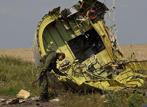 FILE - In this July 22, 2014 file photo, a pro-Russian rebel touches the MH17 wreckage at the crash site of Malaysia Airlines Flight 17, near the village of Hrabove, eastern Ukraine. United by grief across oceans and continents, families who lost loved ones when Malaysia Airlines Flight 17 was shot down in 2014 hope that a trial starting next week will finally deliver them something that has remained elusive ever since: The truth. (AP Photo/Vadim Ghirda, File)