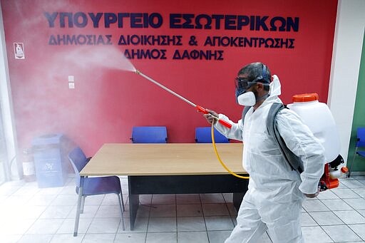 A worker wearing a protective suit sprays disinfectant inside a citizen's service office in the Athens' eastern suburb of Dafni, Monday, March 9, 2020. The sign reads &quot;Interior Ministry. Municipality of Dafni.&quot; (AP Photo/Thanassis Stavrakis)