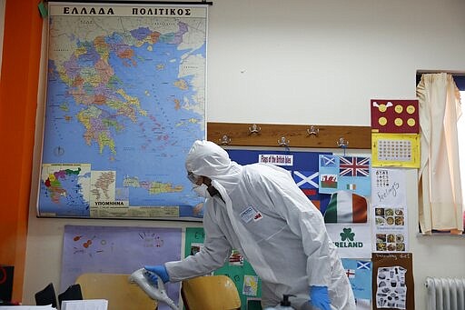 A worker wearing protective suit sprays disinfectant inside a classroom at a primary school in Athens, Monday, March 9, 2020. (AP Photo/Thanassis Stavrakis)