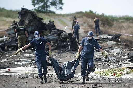 FILE - In this Sunday, July 20, 2014 file photo Ukrainian Emergency workers carry a victim's body in a body bag as pro-Russian fighters stand guard at the crash site of Malaysia Airlines Flight MH17 near the village of Hrabove, eastern Ukraine, killing 298 people. United by grief across oceans and continents, families who lost loved ones when Malaysia Airlines Flight 17 was shot down in 2014 hope that a trial starting next week will finally deliver them something that has remained elusive ever since: The truth. (AP Photo/Evgeniy Maloletka, file)