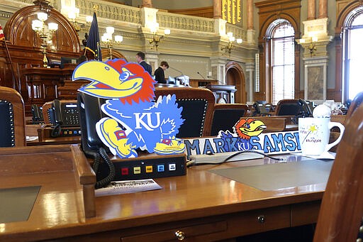 The desk of Kansas state Rep. Mark Samsel, R-Wellsville, honors University of Kansas sports teams with a sign depicting the Jayhawk mascot, Tuesday, March 10, 2020, on his House chamber desk of the Statehouse in Topeka, Kan. Kansas lawmakers are considering legislation to allow college athletes to hire agents and sign endorsement deals. (AP Photo/John Hanna)