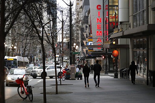 In this March 6, 2020 photo, people walk on a sidewalk on Pike St. in downtown Seattle at 5:20pm during the Friday evening commute. Many of the region's big employers, including Microsoft and Amazon, have started asking workers to stay home and work remotely, and while the closures may help prevent the spread of the COVID-19 coronavirus, it also throws restaurants, shops and hotels into uncertainty. (AP Photo/Ted S. Warren)