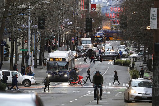 In this March 6, 2020 photo, bus, bike, pedestrian and car traffic is light on Pike St. in downtown Seattle at 5:20 pm during the Friday evening commute. Many of the region's big employers, including Microsoft and Amazon, have started asking workers to stay home and work remotely, and while the closures may help prevent the spread of the COVID-19 coronavirus, it also throws restaurants, shops and hotels into uncertainty. (AP Photo/Ted S. Warren)