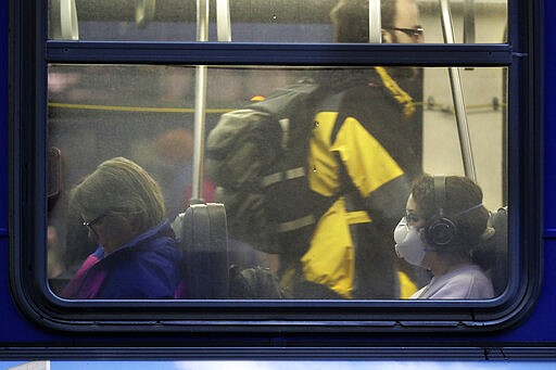 In this March 6, 2020 photo, a woman wears a mask as she rides a bus in downtown Seattle during the Friday evening commute. Many of the region's big employers, including Microsoft and Amazon, have started asking workers to stay home and work remotely, and while the closures may help prevent the spread of the COVID-19 coronavirus, it also throws restaurants, shops and hotels into uncertainty. (AP Photo/Ted S. Warren)