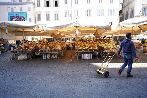 A man pulls a trolley at an emtpy Campo dei Fiori open-air market, in Rome, Tuesday, March 10, 2020. The Italian government is assuring its citizens that supermarkets will remain open and stocked after panic buying erupted after broad anti-virus measures were announced nationwide, sparking overnight runs on 24-hour markets. (AP Photo/Andrew Medichini)