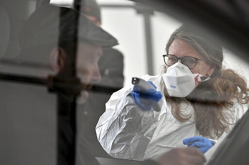 A member of the medical staff measures the temperature of a traveller at a autobahn park place near Gries am Brenner, Austrian province of Tyrol, at border crossing with Italy on Tuesday, March 10, 2020. Austria authorities started on random checks of arriving vehicles at the border crossings with Italy in reaction to the outbreak of the new coronavirus in Europe, particularly in Italy. As part of the move, officials measure the temperatures of some passengers in cars, trucks and buses. For most people, the new coronavirus causes only mild or moderate symptoms, such as fever and cough. For some, especially older adults and people with existing health problems, it can cause more severe illness, including pneumonia. (AP Photo/Kerstin Joensson )