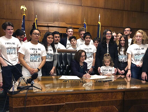 Oregon Gov. Kate Brown signs an executive order on Tuesday, March 10, 2020, ordering the state to lower greenhouse gas emissions, as students look on in Salem, Ore. In an end run around Republican legislators, Oregon's Democratic governor ordered the state on Tuesday to lower greenhouse gas emissions, directing a state agency to set and enforce caps on pollution from industry and transportation fuels. (AP Photo/Andrew Selsky)