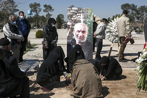 Relatives wearing face masks mourn over the grave of former politburo official in the Revolutionary Guard Farzad Tazari, shown in poster, who died Monday after being infected with the new coronavirus, at the Behesht-e-Zahra cemetery just outside Tehran, Iran, Tuesday, March 10, 2020. Iran is the hardest-hit country in the Mideast by the new coronavirus, which sickens but largely doesn't kill those afflicted. (Mahmood Hosseini/Tasnim News Agency via AP)