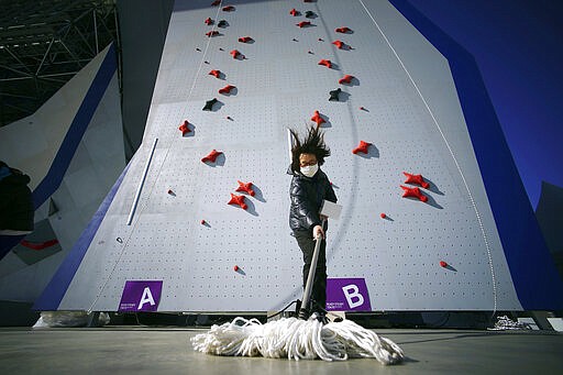 FILE - In this March 6, 2020, file photo, a Tokyo 2020 Olympic Games Organizing staff mops the floor in front of the climbing wall in the test event of Speed Climbing in preparation for the Tokyo 2020 Olympic Games at Aomi Urban Sports Park in Tokyo. The tentacles of cancelling the Tokyo Olympics &#151; or postponing or staging it in empty venues &#151; would reach into every corner of the globe, much like the spreading virus that now imperils the opening ceremony on July 24. (AP Photo/Eugene Hoshiko, File)