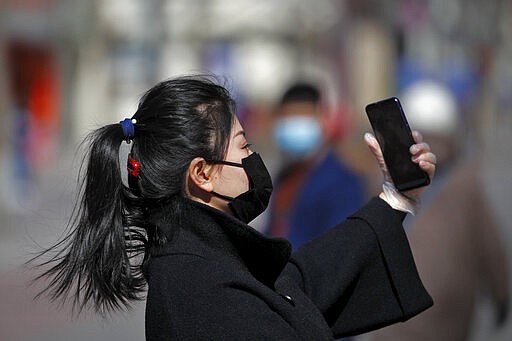 A masked woman wearing a hand glove takes a selfie at the Wangfujing shopping district in Beijing, Tuesday, March 10, 2020. For most people, the new coronavirus causes only mild or moderate symptoms, such as fever and cough. For some, especially older adults and people with existing health problems, it can cause more severe illness, including pneumonia. (AP Photo/Andy Wong)