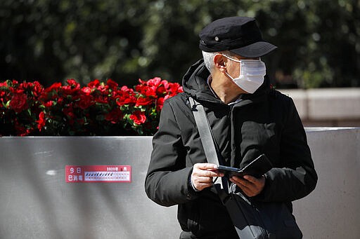 A man wearing a protective face mask sits on a bench with a disinfectant notice at the Wangfujing shopping district in Beijing, Tuesday, March 10, 2020. For most people, the new coronavirus causes only mild or moderate symptoms, such as fever and cough. For some, especially older adults and people with existing health problems, it can cause more severe illness, including pneumonia. (AP Photo/Andy Wong)