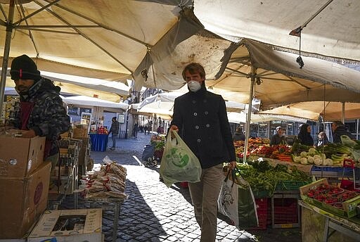 A man wears a mask as he carries his groceries at Campo dei Fiori open-air market, in Rome, Tuesday, March 10, 2020. The Italian government is assuring its citizens that supermarkets will remain open and stocked after panic buying erupted after broad anti-virus measures were announced nationwide, sparking overnight runs on 24-hour markets. (AP Photo/Andrew Medichini)