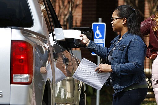 Amour Fowler, a Jackson, Miss., precinct poll manager delivers a ballot to a curbside voter in Jackson, Miss., Tuesday, March 10, 2020. Mississippi is one of several states holding presidential party primaries today. (AP Photo/Rogelio V. Solis)