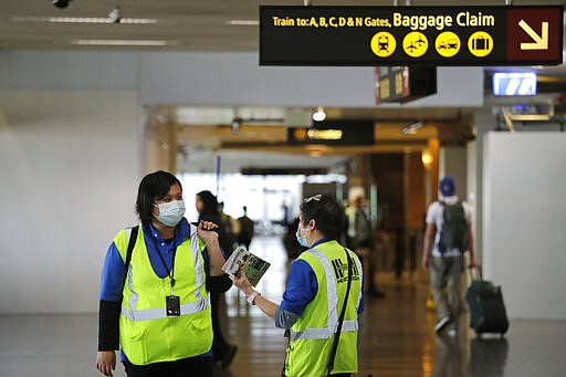 FILE - In this Tuesday, March 3, 2020, file photo, a pair of workers at Seattle-Tacoma International Airport wear masks in SeaTac, Wash. While white collar workers trying to avoid contagion can work from home or call in sick if they experience symptoms of the new virus, such precautions are not an options for the millions of waiters, delivery workers, cashiers, ride-hailing drivers, museum attendants and countless others who routinely come into contact with the public. (AP Photo/Elaine Thompson, File)