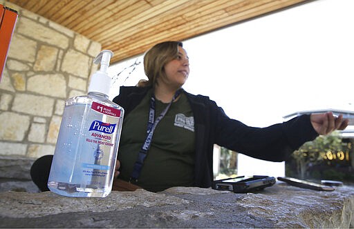 In this photo made Friday, March 6, 2020, a bottle of hand sanitizer sits next to ticket taker Mariah Bernal as she hands back tickets to a patron entering the Dallas Zoo in Dallas. While white collar workers trying to avoid contagion can work from home or call in sick if they experience symptoms of the new virus, such precautions are not an options for the millions of waiters, delivery workers, cashiers, ride-hailing drivers, museum attendants and countless others who routinely come into contact with the public. (AP Photo/LM Otero)