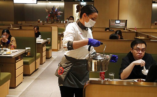 In this March 5, 2020, photo, a waitress of the Chinese restaurant Hot Pot serves customers in London. While white collar workers trying to avoid contagion can work from home or call in sick if they experience symptoms of the virus, such precautions are not an options for the millions of waiters, delivery workers, cashiers, ride-hailing drivers, museum attendants and countless others who routinely come into contact with the public. (AP Photo/Frank Augstein)