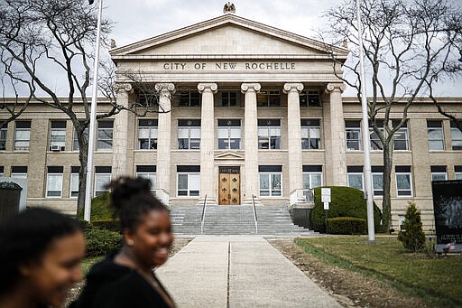 Pedestrians pass New Rochelle City Hall, Tuesday, March 10, 2020, in New York.  State officials are shuttering several schools and houses of worship for two weeks in the New York City suburb and sending in the National Guard to help with what appears to be the nation's biggest cluster of coronavirus cases, Gov. Andrew Cuomo said Tuesday.   (AP Photo/John Minchillo)