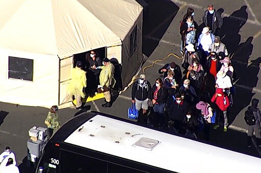 This photo taken from pool video provided by KGO-TV, shows passengers waiting to board buses after leaving the Grand Princess cruise ship at the Port of Oakland, Tuesday, March 10, 2020, in Oakland, Calif.  Passengers wearing masks trickled out of the Grand Princess and walked to the bottom of a ramp, where masked officials in yellow protective gear and blue plastic gloves took their temperature and led them to a tent for more screening before they lined up to board a bus to quarantine. (KGO-TV via AP, Pool)