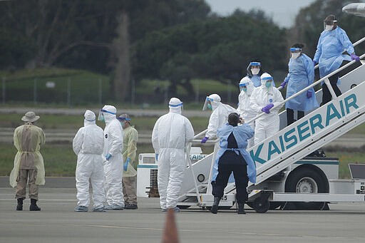 Workers in protective clothing wait for passengers from the Grand Princess, a cruise ship carrying multiple people who have tested positive for COVID-19, to board a chartered plane in Oakland, Calif., Tuesday, March 10, 2020. The passengers on the flight are going to San Antonio to be quarantined at Lackland Air Force Base. (AP Photo/Jeff Chiu)