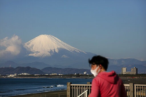 FILE - In this Feb. 27, 2020, file photo, a man wearing a mask visits a beach as snow-capped Mount Fuji is visible in the distance in Fujisawa, Japan. The tentacles of cancelling the Tokyo Olympics &#151; or postponing or staging it in empty venues &#151; would reach into every corner of the globe, much like the spreading virus that now imperils the opening ceremony on July 24. (AP Photo/Jae C. Hong, File)