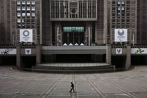 FILE - In this Feb. 25, 2020, file photo, man walks in front of the Tokyo Metropolitan Government building adorned with large banners promoting the Tokyo 2020 Olympics and Paralympics in Tokyo. The tentacles of cancelling the Tokyo Olympics &#151; or postponing or staging it in empty venues &#151; would reach into every corner of the globe, much like the spreading virus that now imperils the opening ceremony on July 24. (AP Photo/Jae C. Hong, File)