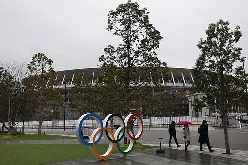 FILE - In this March 4, 2020, file photo, people walk past the Olympic rings near the New National Stadium in Tokyo. The tentacles of cancelling the Tokyo Olympics &#151; or postponing or staging it in empty venues &#151; would reach into every corner of the globe, much like the spreading virus that now imperils the opening ceremony on July 24. (AP Photo/Jae C. Hong, File)