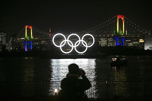 FILE - In this Jan. 24, 2020, file photo, a photographer takes pictures of the illuminated Olympic rings in front of the Rainbow Bridge Friday, Jan. 24, 2020, in the Odaiba district of Tokyo. The tentacles of cancelling the Tokyo Olympics &#151; or postponing or staging it in empty venues &#151; would reach into every corner of the globe, much like the spreading virus that now imperils the opening ceremony on July 24. (AP Photo/Jae C. Hong, File)