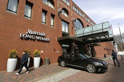 People walk outside the Marriott Long Wharf hotel, Wednesday, March 11, 2020, in Boston. Seventy of Massachusetts' first 92 confirmed coronavirus cases have been linked to a meeting of Biogen executives that was held at the hotel in late February 2020. For most people, the virus causes only mild or moderate symptoms, such as fever and cough. For some, especially older adults and people with existing health problems, it can cause more severe illness, including pneumonia. The vast majority of people recover from the new virus. (AP Photo/Steven Senne)