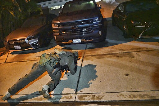 A DEA agent checks under a car at a residential house during an arrest of a suspected drug trafficker on Wednesday, March 11, 2020 in Diamond Bar, Calif. In early-morning raids Wednesday, federal agents fanned out across the U.S., culminating a six-month investigation with the primary goal of dismantling the upper echelon of the Jalisco New Generation Cartel, known as CJNG. (AP Photo/Richard Vogel)