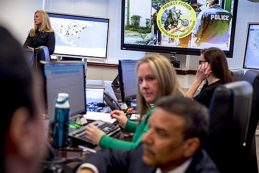 DEA agents and intelligence analysts take information from field operations as Wendy Woolcok, the special agent in charge of the Drug Enforcement Administration's special operations division, top left, stands next to a monitor displaying arrests made across the country as part of &quot;Project Python&quot; at their command center in Chantilly, Va., Wednesday, March 11, 2020. (AP Photo/Andrew Harnik)