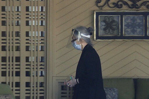 A worker wears a mask and a protective face shield as she walks into the Life Care Center in Kirkland, Wash. Monday, March 9, 2020, near Seattle. The nursing home is at the center of the outbreak of the COVID-19 coronavirus in Washington state. (AP Photo/Ted S. Warren)