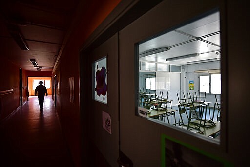 A teacher walks along a hallway of an empty public school in small Spanish Basque village of Labastida, around 45 kms (24,85 miles) from Vitoria, northern Spain, Wednesday, March 11, 2020. Spain's health minister on Monday announced a sharp spike in coronavirus cases in and around the national capital, and said all schools in the region, including kindergartens and universities, and the same in the Spanish Basque city of Vitoria, will close for two weeks.For most people, the new coronavirus causes only mild or moderate symptoms, such as fever and cough. For some, especially older adults and people with existing health problems, it can cause more severe illness, including pneumonia. (AP Photo/Alvaro Barrientos)