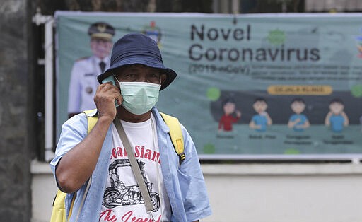 A man wears a face mask as he talks on his mobile phone near a banner promoting awareness of the coronavirus outbreak in Medan, North Sumatra, Indonesia, Wednesday, March 11, 2020.  The vast majority of people recover from the new virus. According to the World Health Organization, people with mild illness recover in about two weeks, while those with more severe illness may take three to six weeks to recover. In mainland China, where the virus first exploded, more than 80,000 people have been diagnosed and more than 58,000 have so far recovered. (AP Photo/Binsar Bakkara)