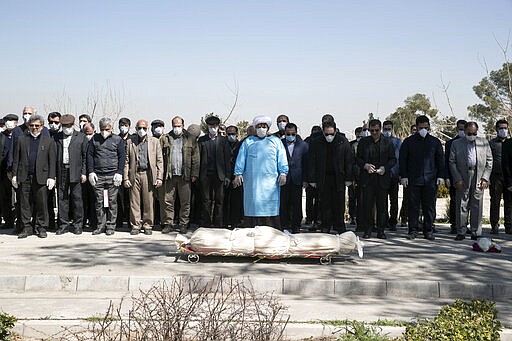 Mourners wearing face masks and gloves pray over the body of former politburo official in the Revolutionary Guard Farzad Tazari, who died Monday after being infected with the new coronavirus, at the Behesht-e-Zahra cemetery just outside Tehran, Iran, Tuesday, March 10, 2020. Iran is the hardest-hit country in the Mideast by the new coronavirus, which sickens but largely doesn't kill those afflicted. (Mahmood Hosseini/Tasnim News Agency via AP)