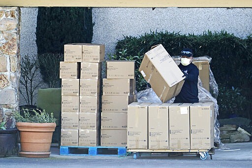 A worker at the Life Care Center in Kirkland, Wash., wears a mask as he stacks newly arrived boxes of gloves, gowns, and other protective gear on a cart, Monday, March 9, 2020, near Seattle. The nursing home is at the center of the outbreak of the new coronavirus in Washington state. (AP Photo/Ted S. Warren)