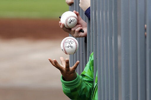 A child tosses an already-autographed baseball while awaiting another signature from a passing player before a spring training baseball game between the Los Angeles Angels and the Seattle Mariners on Tuesday, March 10, 2020, in Peoria, Ariz. (AP Photo/Elaine Thompson)