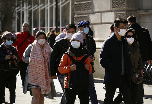 People wear protective face masks as they walk outside Parliament in London, Wednesday, March 11, 2020. A British government minister Nadine Dorries, who is a junior Heath minster has tested positive for the coronavirus and is self isolating. For most people, the new coronavirus causes only mild or moderate symptoms, such as fever and cough. For some, especially older adults and people with existing health problems, it can cause more severe illness, including pneumonia. (AP Photo/Matt Dunham)