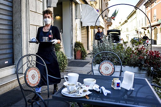 A waitress wears a mask and gloves as she carries a tray at a cafe in the town of Codogno, in the region of Lombardia, northern Italy, Wednesday, March 11, 2020. The Lombardy cluster of COVID-19 was first registered in the tiny town of Codogno on Feb. 19, when the first patient tested positive and has been a red zone until the end of seclusion and return of production in the recent days. For most people, the new coronavirus causes only mild or moderate symptoms, such as fever and cough. For some, especially older adults and people with existing health problems, it can cause more severe illness, including pneumonia. (Claudio Furlan/LaPresse via AP)