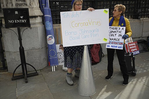 Anti Brexit campaigners hold placards including comments on the outbreak of coronavirus as they protest outside Parliament in London, Wednesday, March 11, 2020. A British government minister Nadine Dorries, who is a junior Heath minster has tested positive for the coronavirus and is self isolating. Britain's Chancellor of the Exchequer Rishi Sunak will announce the first budget since Britain left the European Union.(AP Photo/Matt Dunham)