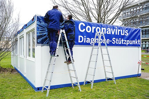 Craftsmen attach a banner with the inscription &quot;Coronavirus Diagnosis Base&quot; to containers set up on the grounds of the University Hospital in Mannheim, Germany, Wednesday, March 11, 2020. Due to the coronavirus epidemic, the University Hospital has established a coronavirus diagnosis and test center. For most people, the new coronavirus causes only mild or moderate symptoms, such as fever and cough. For some, especially older adults and people with existing health problems, it can cause more severe illness, including pneumonia. Uwe Anspach/dpa via AP)