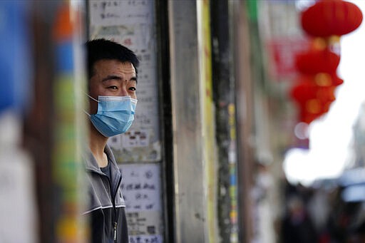 A man wearing a face mask looks out from a supermarket in Madrid, Spain, Wednesday, March 11, 2020. Spain's health minister on Monday announced a sharp spike in coronavirus cases in and around the national capital, Madrid, and said all schools in the region, including kindergartens and universities, will close for two weeks from Wednesday. For most people, the new coronavirus causes only mild or moderate symptoms, such as fever and cough. For some, especially older adults and people with existing health problems, it can cause more severe illness, including pneumonia. (AP Photo/Manu Fernandez)