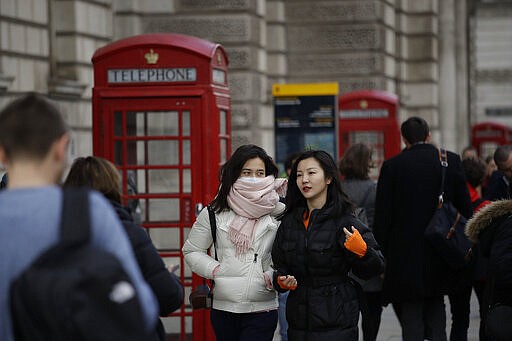 A woman wearing a scarf covering a face mask walks past traditional British red phone boxes near Parliament Square in central London, Wednesday, March 11, 2020. A British government minister Nadine Dorries, who is a junior Heath minster has tested positive for the coronavirus and is self isolating. For most people, the new coronavirus causes only mild or moderate symptoms, such as fever and cough. For some, especially older adults and people with existing health problems, it can cause more severe illness, including pneumonia. (AP Photo/Matt Dunham)