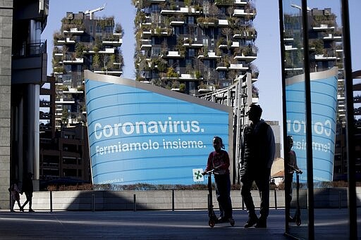 A man and a girl on a scooter are backdropped by a Lombardy region campaign advertising reading in Italian ' Coronavirus let's stop it together ', at the Porta Nuova business district in Milan, Wednesday, March 11, 2020. Italy is mulling even tighter restrictions on daily life and has announced billions in financial relief to cushion economic shocks from the coronavirus. For most people, the new coronavirus causes only mild or moderate symptoms, such as fever and cough. For some, especially older adults and people with existing health problems, it can cause more severe illness, including pneumonia. (AP Photo/Luca Bruno)